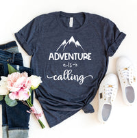 Thumbnail for A navy blue Adventure Is Calling T-shirt shown siting on a white table with jeans pink flowers and white shoes sitting next to it